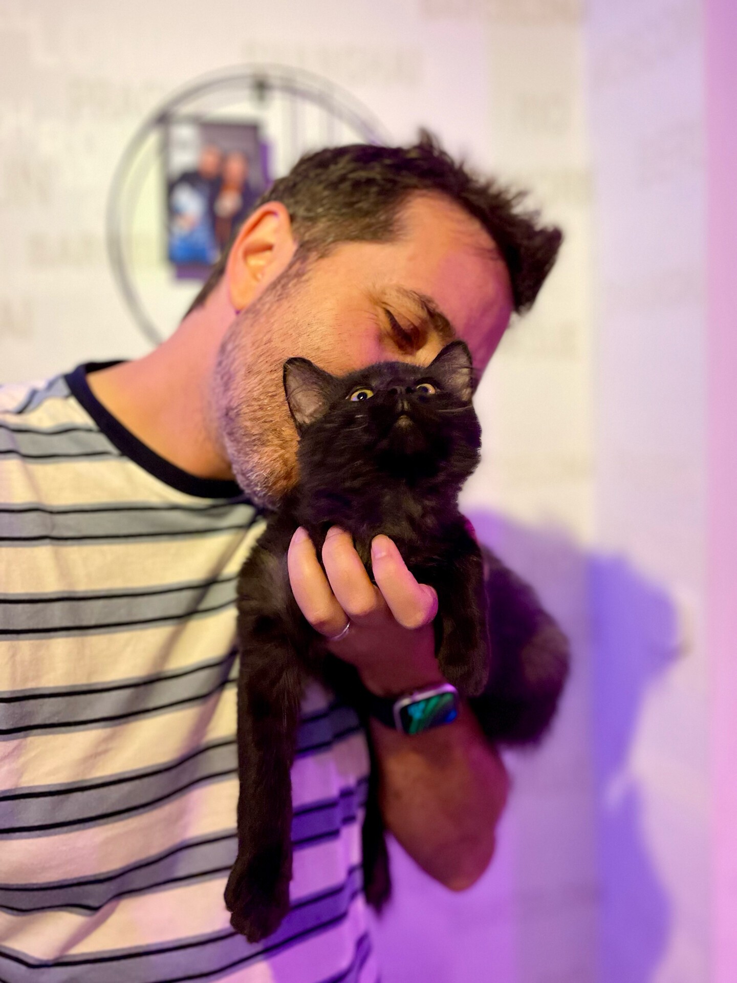 Photo d'un chaton noir en train de se faire embrasser gouleusement par son propriétaire. 
Le chaton à les yeux levés au ciel
