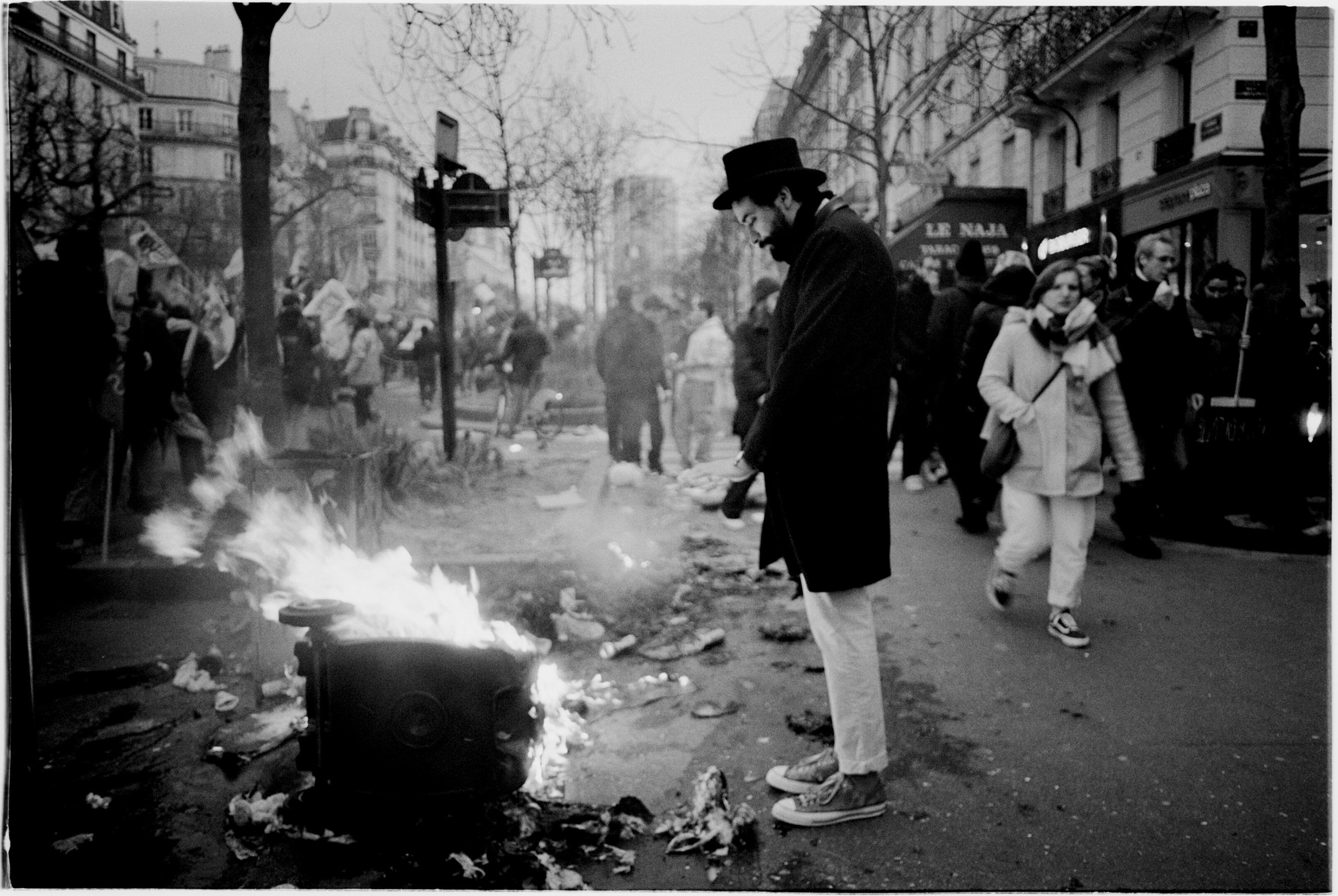man with a hat warming up his hands on a garbage fire during a protest in Paris, march 2023. Black and white photography