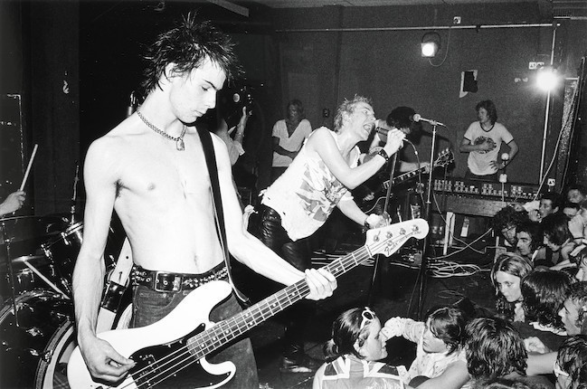 Black and white photography of punk band Sex Pistols. One front Sid Vicious pretending to play bass and behind Johnny Rotten is singing holding firmly his mile