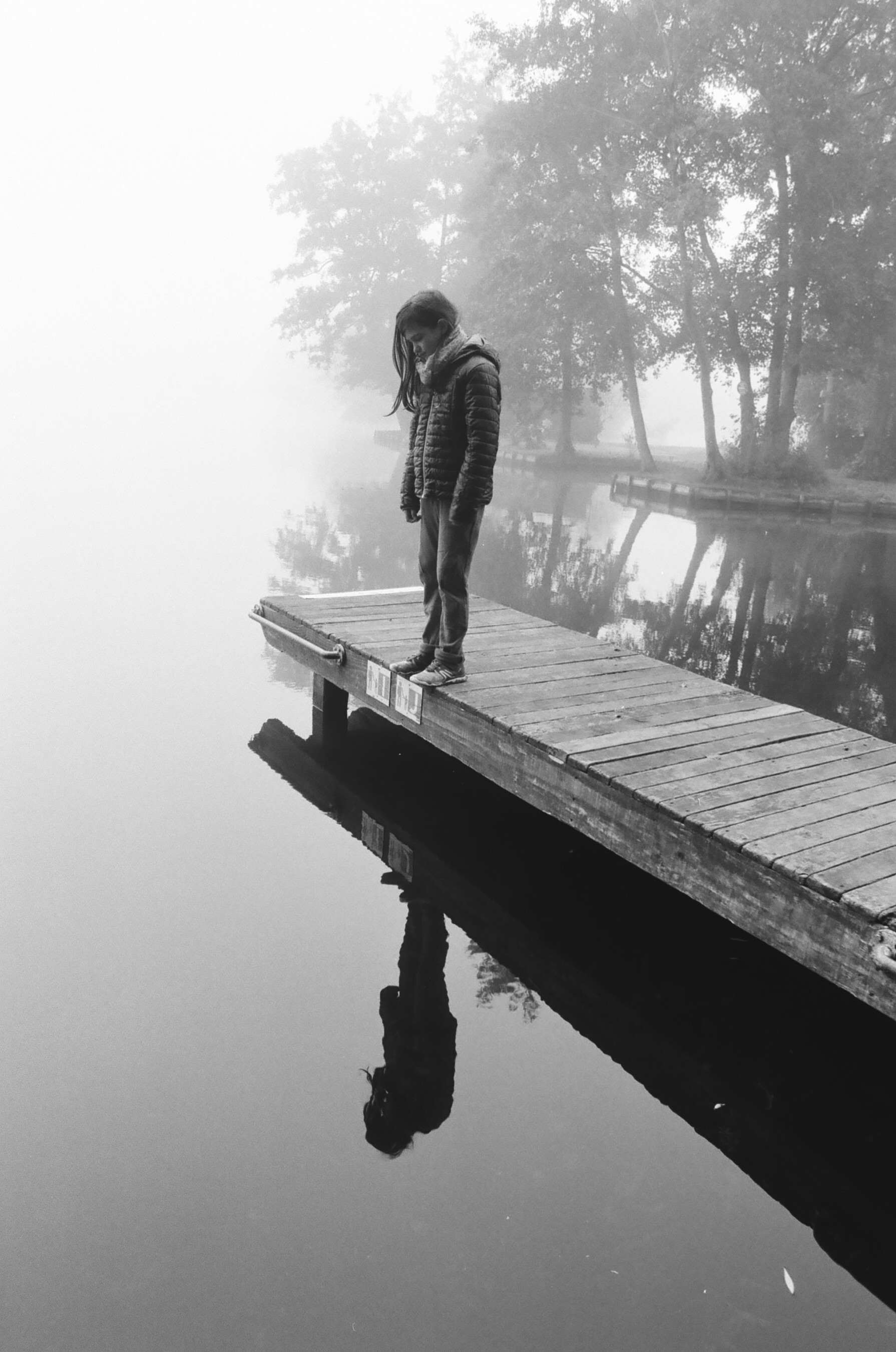 une fille sur un ponton dans la brume regarde son reflet dans un lac