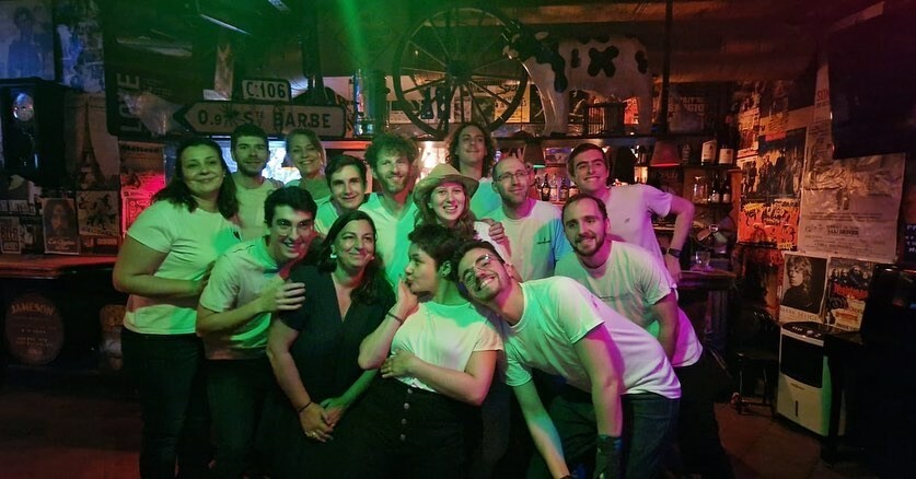 Une troupe pose pour une photo dans un bar. Presque tout le monde est habillé en T-Shirt blanc.