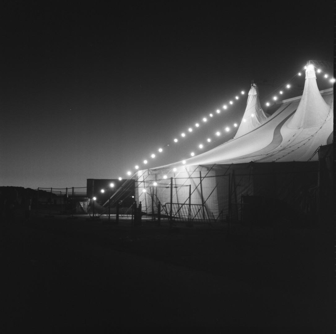 Photos noir et blanc de nuit d'un chapiteau de cirque avec des guirlandes allumé qui font des lignes de point très lumineux.