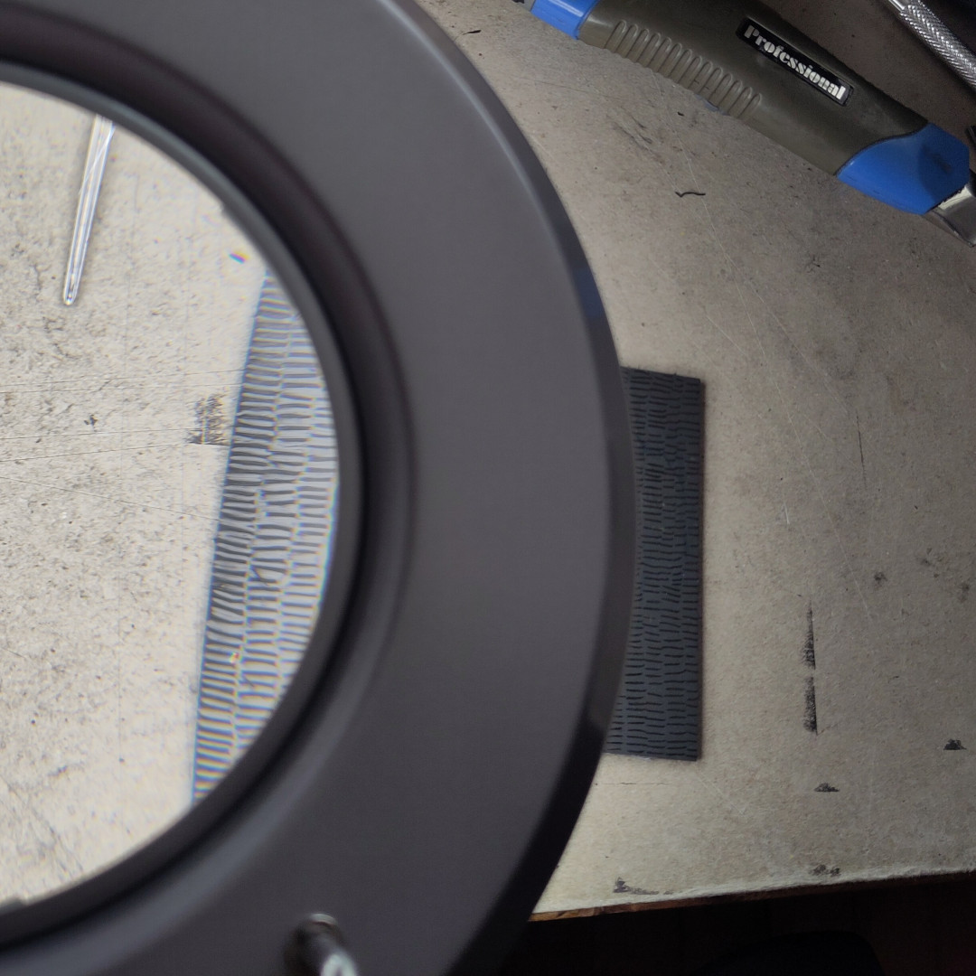 la même plaque, vue d'en haut à travers la grosse loupe lumineuse que j'utilise pour graver
on voit une partie de la plaque grossie par le verre de la loupé, et l'autre partie à taille réelle en dehors de la lentille