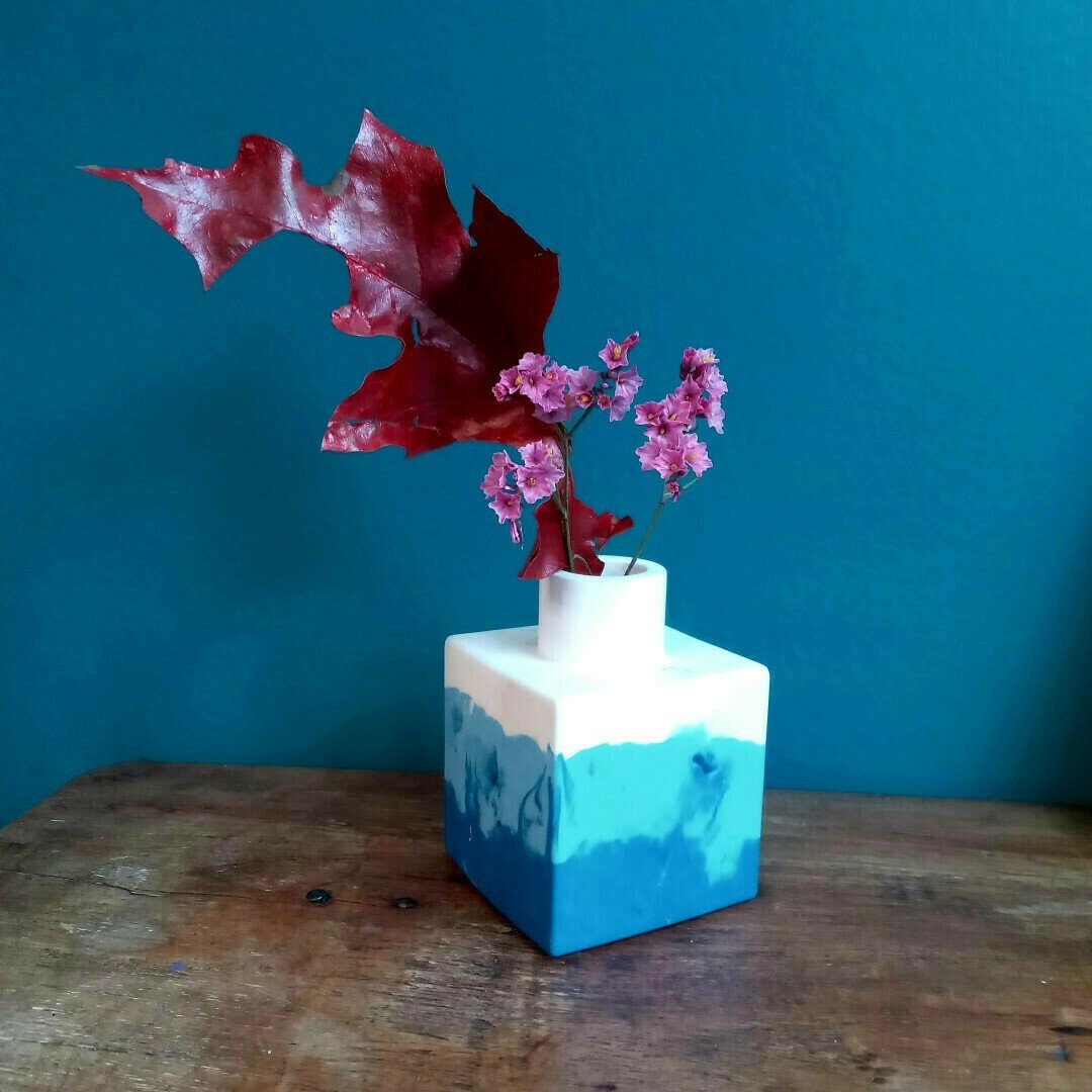 Un petit vase carré blanc et bleu, contenant une grande feuille rouge.