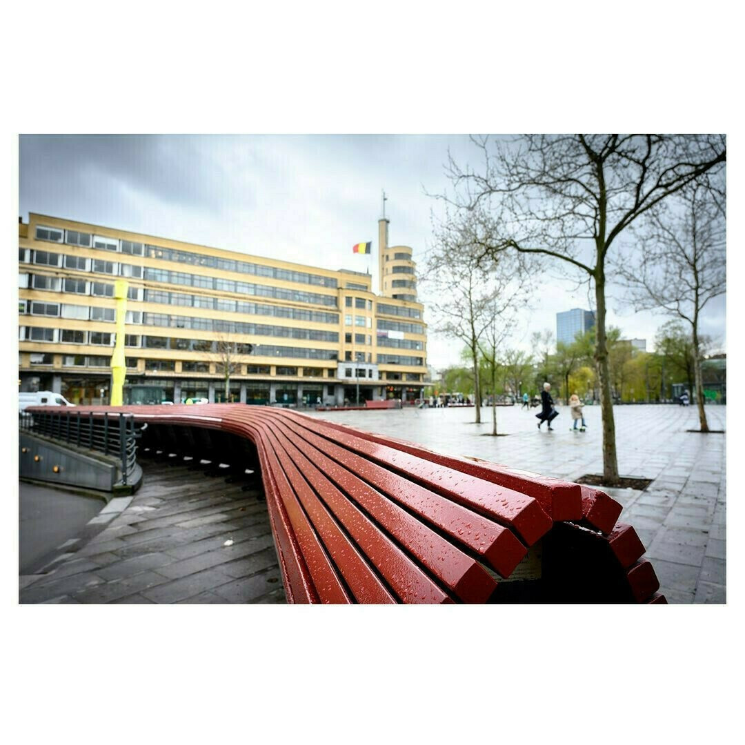 Un banc rouge au premier plan avec un bâtiment en arrière plan, vue grand angle de la place Flagey à Bruxelles.