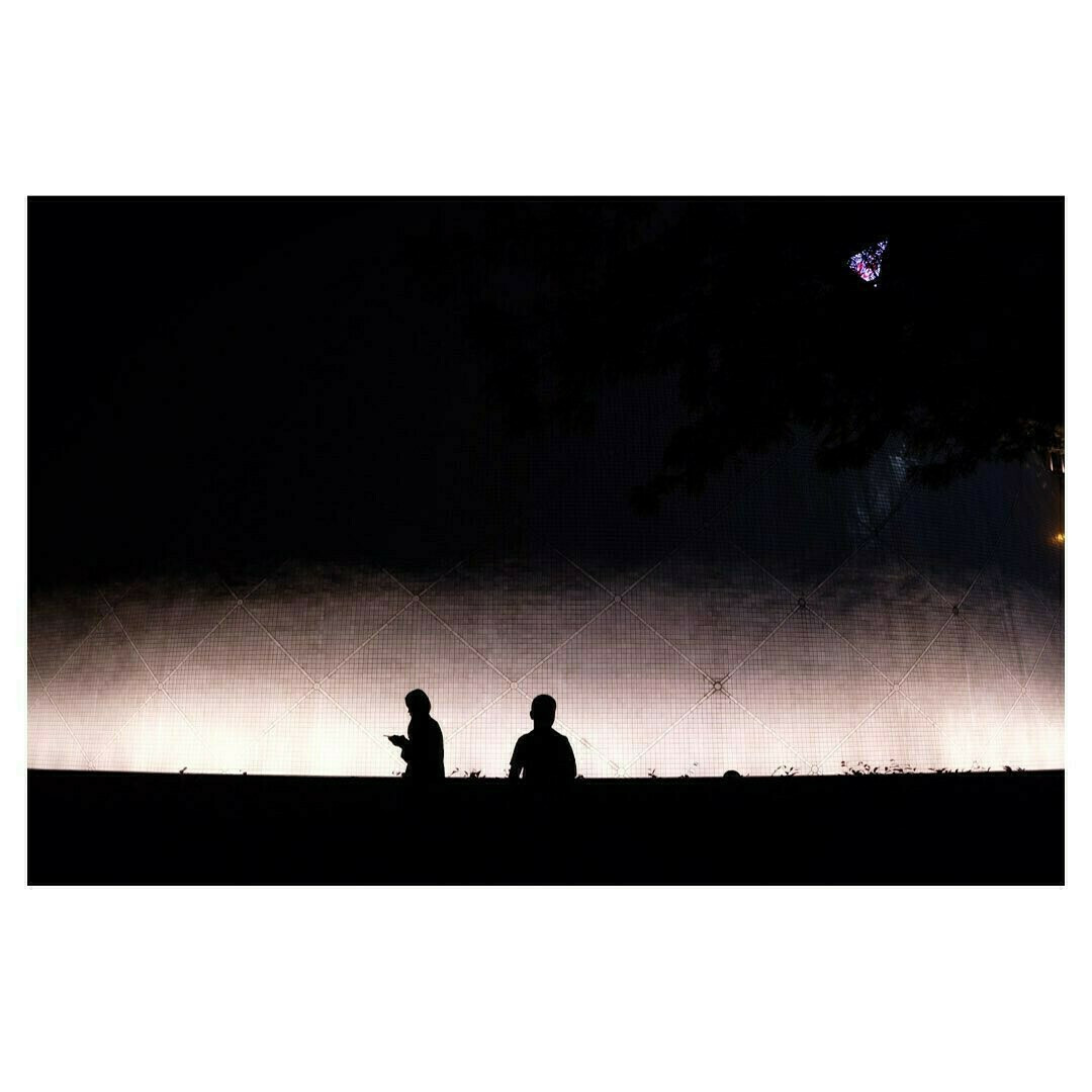 2 silhouettes sur fond sombre, photographiées dans une rue de Hong Kong, la photo montre des ombres pour les deux personnes, les silhouettes, tandis que le second plan est très lumineux.