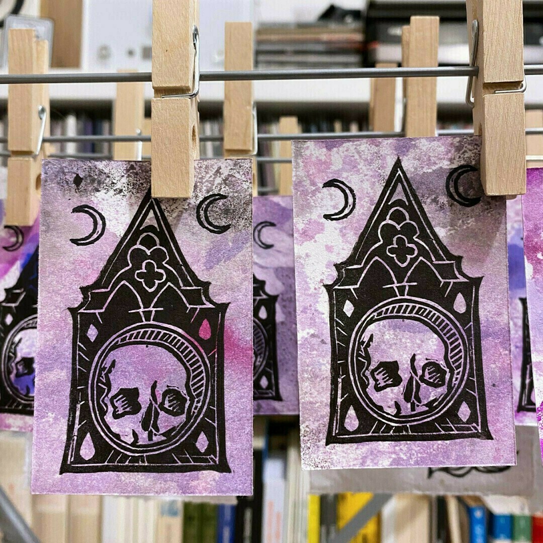 Deux cartes de visite représentant une boîte à crâne et deux croissants de lune, imprimés en noir sur un fond mauve peint à la gouache.