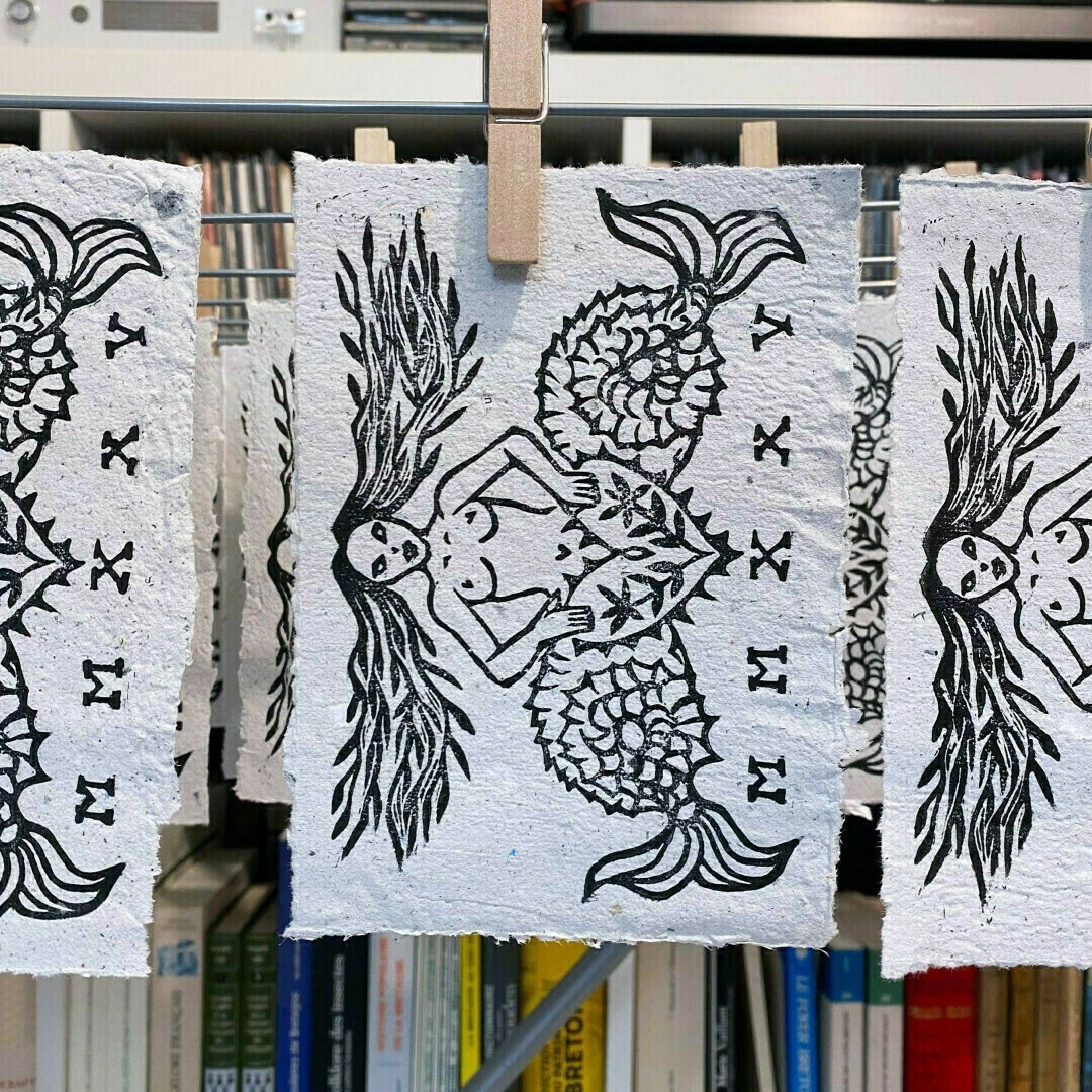 Sirène à deux queues imprimée sur papier recyclé gris.