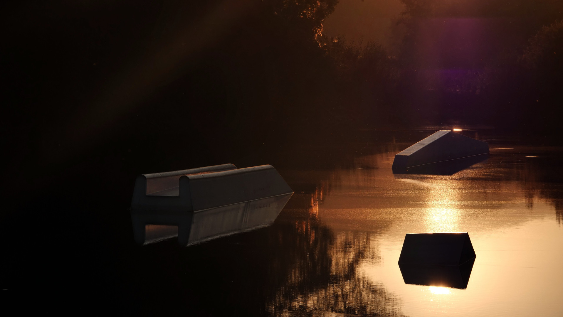 en contre jour des volumes géométriques émerge d'un étang baigné d'une lumière orangée au coucher du soleil