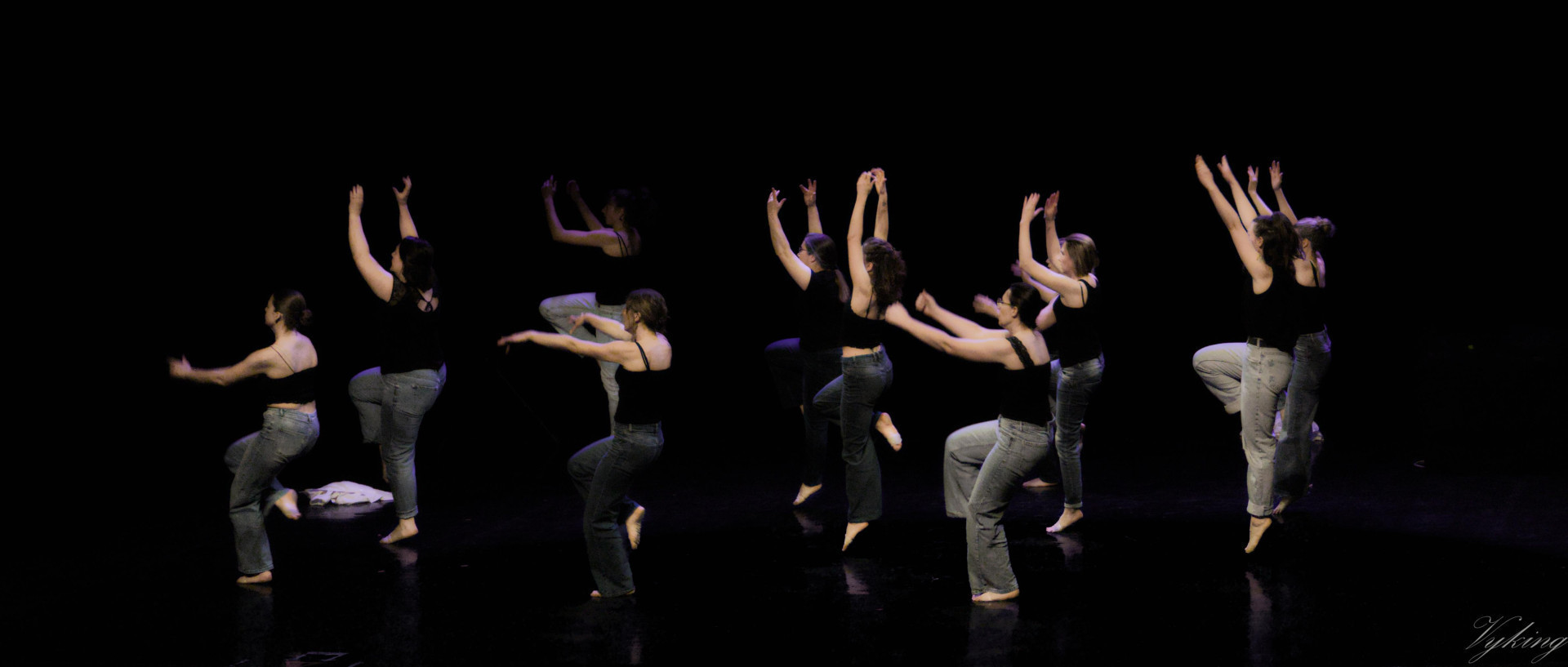 les 10 danseuses sont de profil ou de de 3/4 dos, tournées vers la gauche. Elles sont sur un pied, pour certaines en l’air, les trois de devant les bras tendus en avant, les autres les bras tendus vers le haut. Vêtues de Jeans bleu et d’un haut sans manche noir, elles ressortent dans une lumière qui n’éclaire qu’elles et laisse tout le reste dans l’obscurité à l’exception de leur reflet qu’on devine sur le sol.