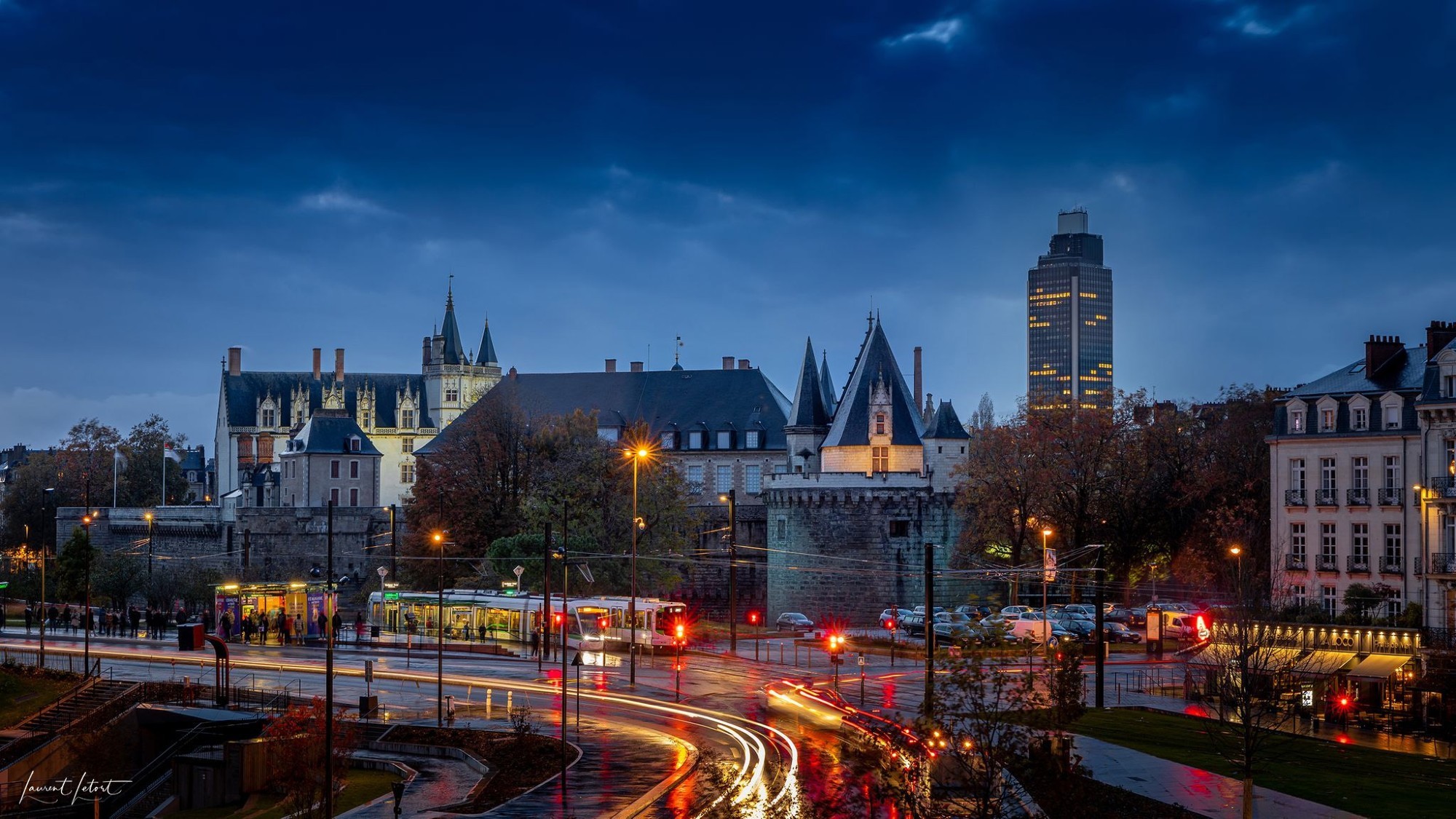 Une vue crépusculaire d'un château historique et d'une tour moderne,  de rues illuminées remplies de tramways et voitures