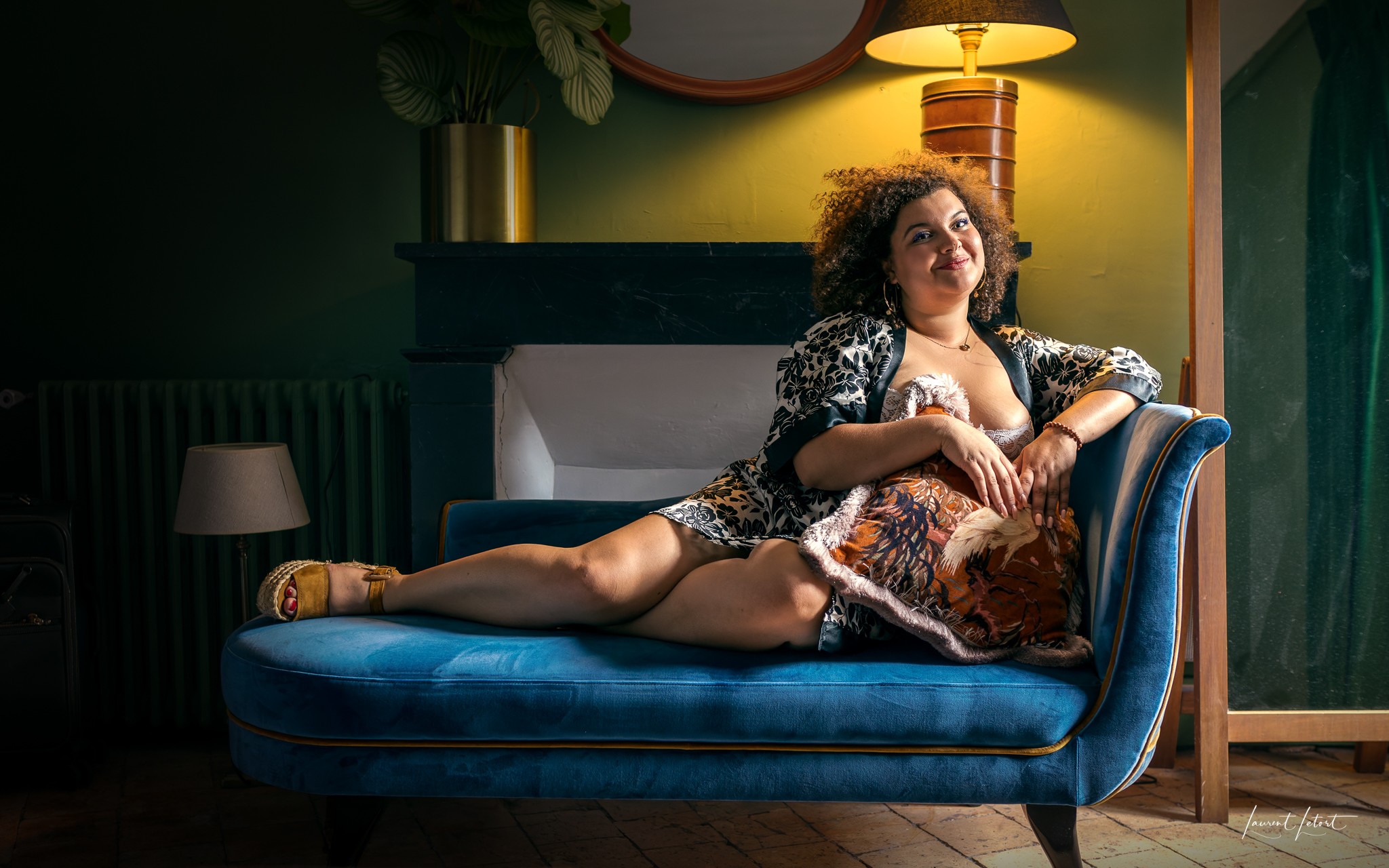 🇫🇷 Une femme se prélasse sur une élégante méridienne bleue, vêtue d'un peignoir à fleurs, dans un éclairage doux et un intérieur douillet.
🇬🇧 A woman lounges on a stylish blue couch, wearing a floral garment, with soft lighting and a cozy interior.